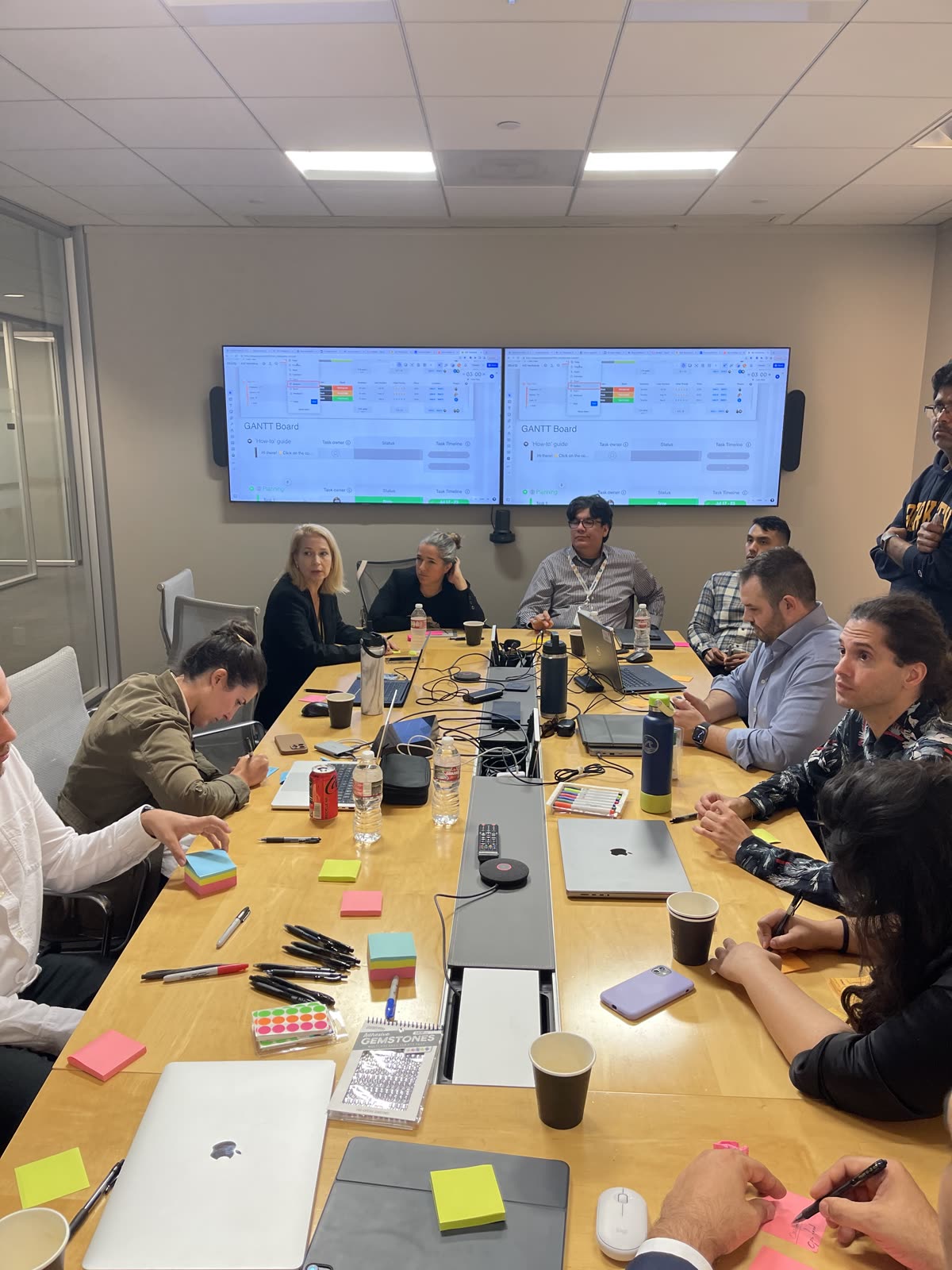 A workshop session in an SLB conference room: the team gathered around a long table, Gantt boards on the wall screens